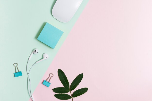 Workspace with earphones and mouse on pink and green background 