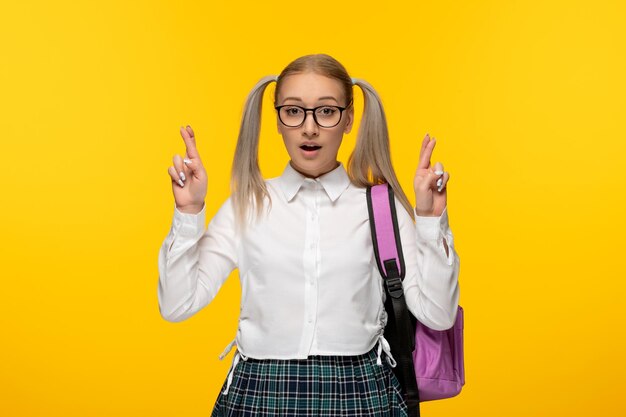 World book day schoolgirl with crossed fingers on yellow background with pink backpack