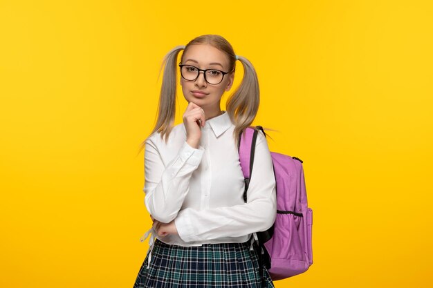 World book day serious schoolgirl in glasses and pink backpack on yellow background