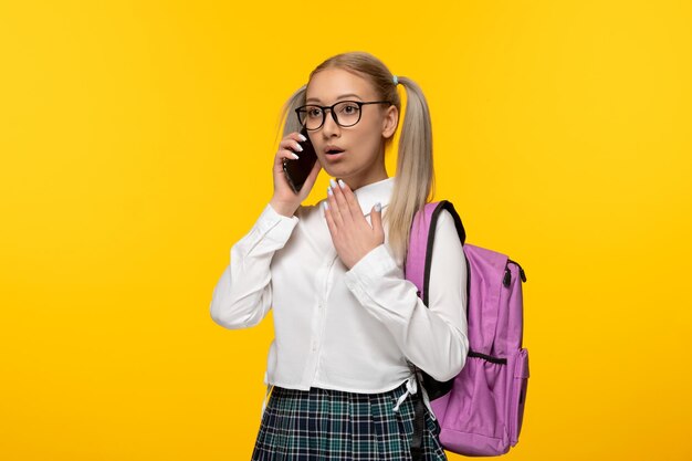 World book day surprised schoolgirl with pink backpack talking on the phone