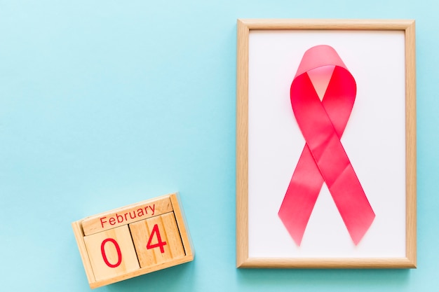Giornata mondiale del cancro il 4 febbraio e cornice in legno con nastro rosa su sfondo blu