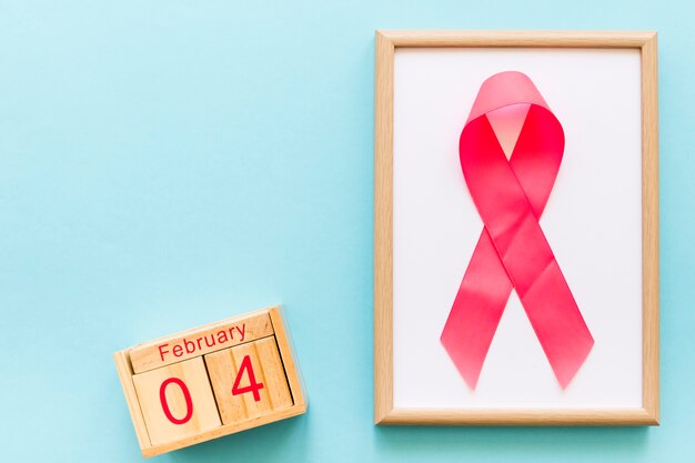 Всемирный день рака 4 февраля и деревянная рамка с розовой лентой на синем фоне