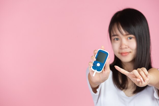 World diabetes day; woman holding Glucose meter on pink wall