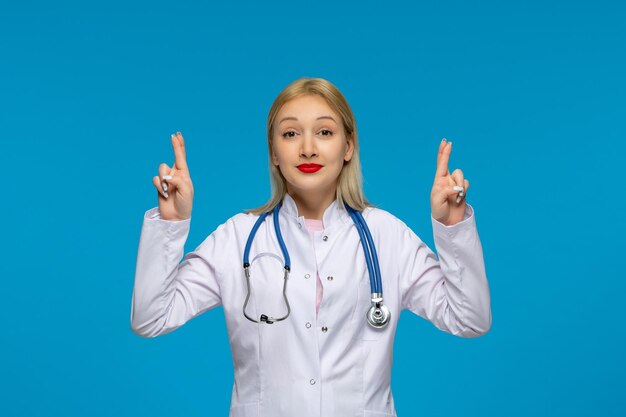 Всемирный день врачей милая блондинка молодой врач скрещивает пальцы со стетоскопом в лабораторном халате