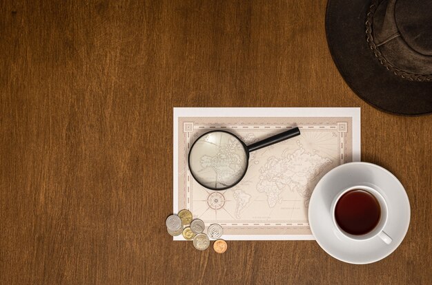 World map, magnifier, money and coffee on wooden background, flat lay, top view, travel concept.