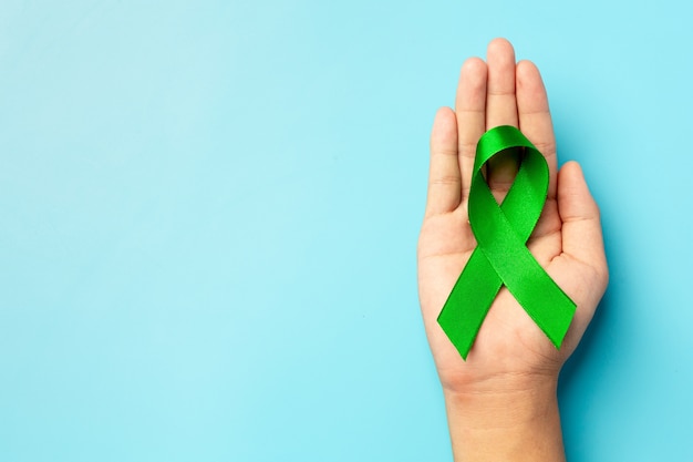 World Mental Health Day. green ribbon put in human's hand on blue background