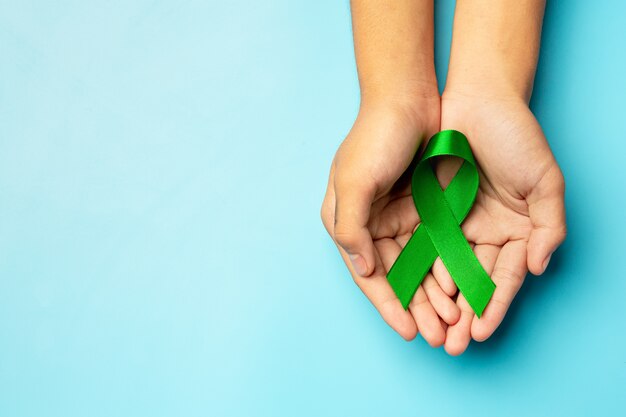 World Mental Health Day. green ribbon put in human's hands on blue background