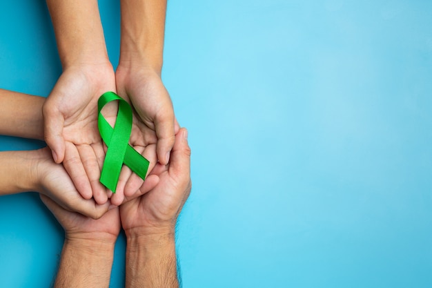 Всемирный день психического здоровья. зеленая лента в руках человека на синем фоне