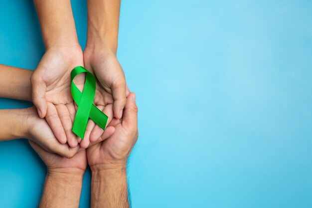 World Mental Health Day. green ribbon put in human's hands on blue background