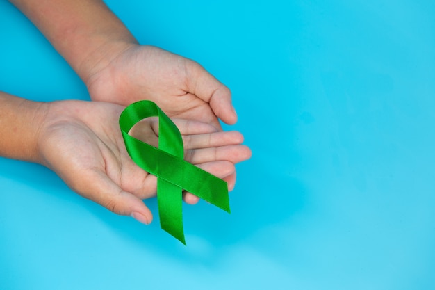 World Mental Health Day. green ribbon put in human's hands on blue background