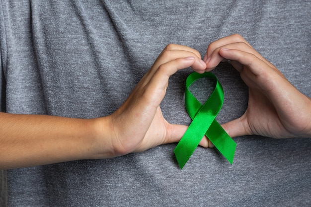World Mental Health Day. man's hand showing heart-shaped around a green ribbon