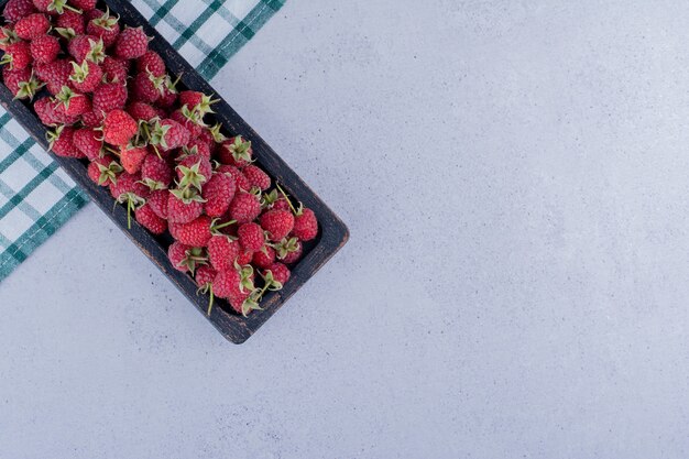 Worn-out black tray filled with raspberries on marble background. High quality photo