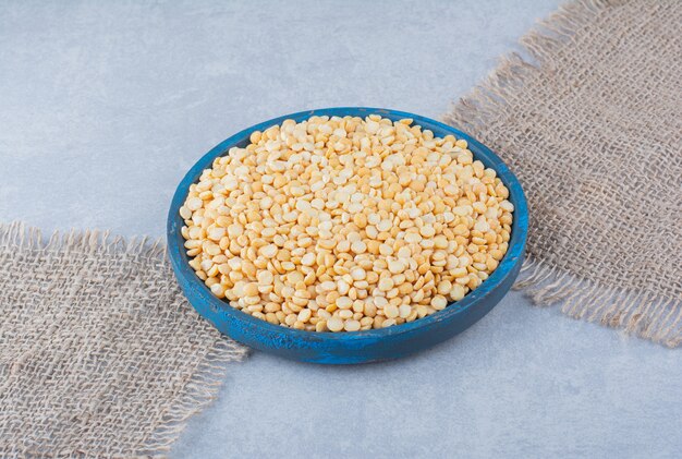 Free photo worn-out blue platter filled with lentils on pieces of fabric on marble background.