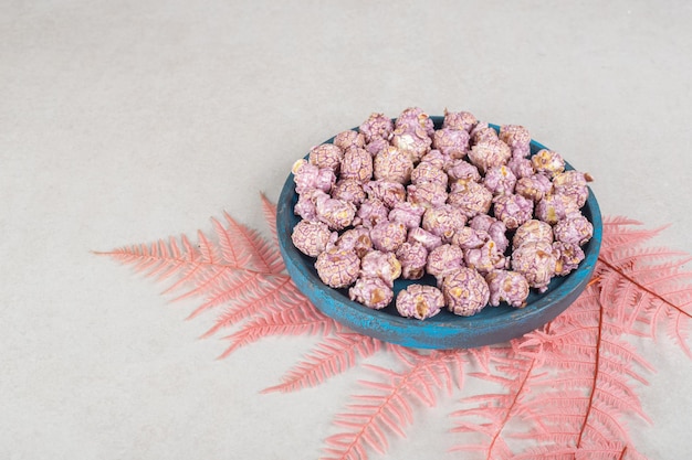 Free photo worn-out wooden tray of flavored popcorn resting on a bunch of pink leaves on marble table.