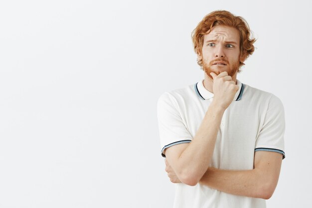 Worried bearded redhead guy posing against the white wall