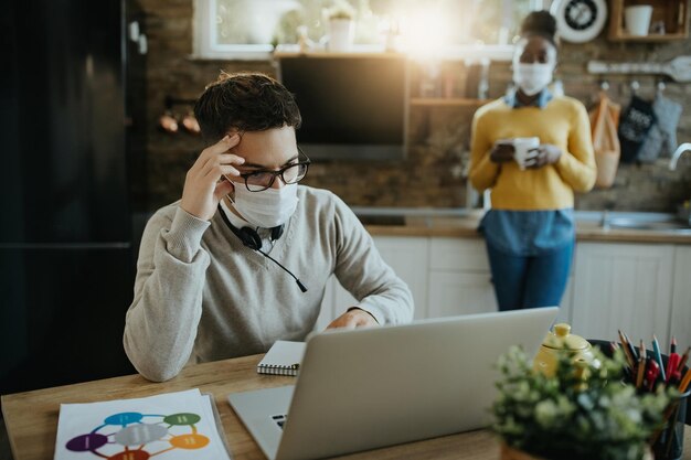 Worried businessman with face mask reading problematic email on laptop at home