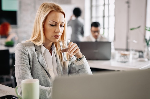 Worried businesswoman working on a computer while drinking water from a glass in the office