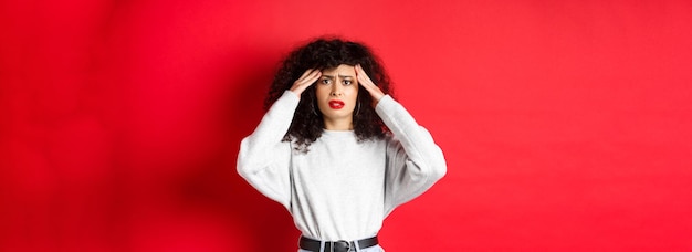 Worried and concerned young woman touching head and grimacing having headache standing with migraine