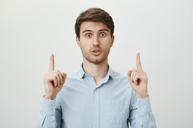 Worried confused guy pointing fingers up, asking question about promo