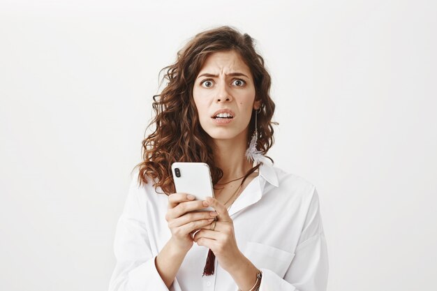 Взволнованная и смущенная женщина читает странное сообщение по мобильному телефону