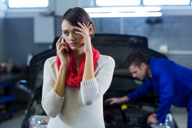 Free photo worried customer talking on mobile phone while mechanic examining car in background