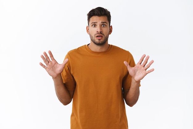 Worried cute bearded guy in tshirt raise hands up in stop gesture shaking hands nervously anxious as being late with buying present frowning sad and indecisive standing white background upset