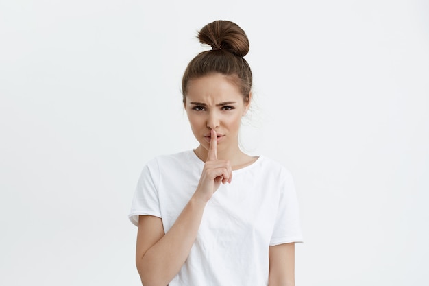 Free photo worried cute european woman holding index finger over lips, asking stay quiet while frowning