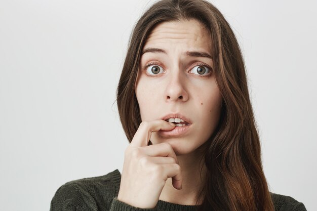 Worried cute woman biting finger, look indecisive