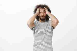 Free photo worried desperate aduly male freelancer with afro haircut in trendy striped t-shirt, holding hands on head and lifting eyebrown, feeling nervous and shocked