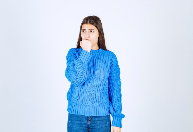 Взволнованная модель девушки в теплом свитере кусает пальцы и смотрит вперед.