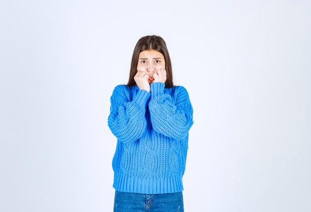 Worried girl model in warm sweater biting her fingers and looking forward.