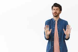 Free photo worried guy doesnt like how offer sounds, trying avoid bad affairs, shaking hands in no reply, rejecting or refusing something suspicious and awful, cringe from aversion or dislike, white wall