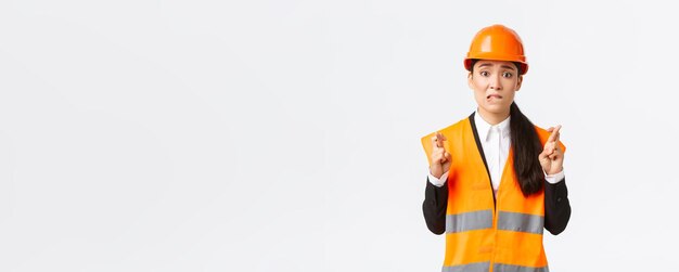 Worried hopeful asian female architect feeling nervous as waiting for inspection results at construction area wearing safety helmet cross fingers good luck hope everything be well