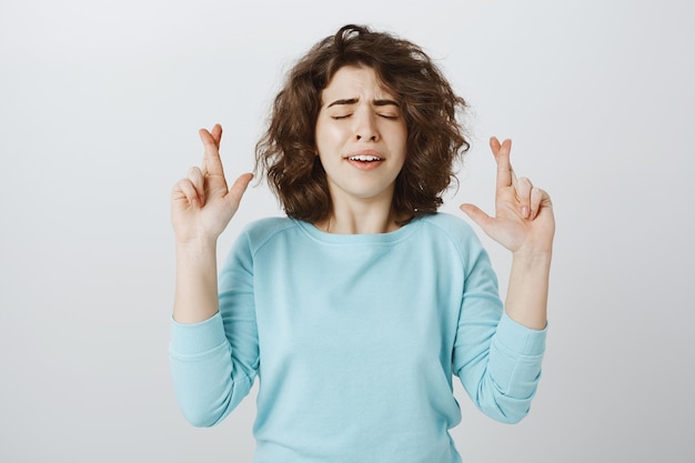 Foto gratuita preoccupata ragazza speranzosa che prega, chiudi gli occhi e incrocia le dita per buona fortuna, esprimendo un desiderio