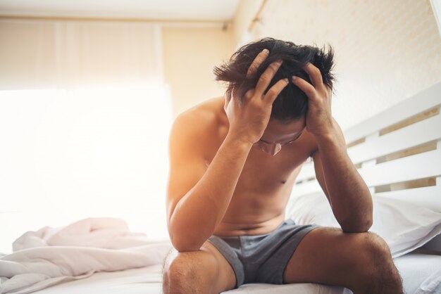 Worried man sitting on bed in the morning, serious thinking something
