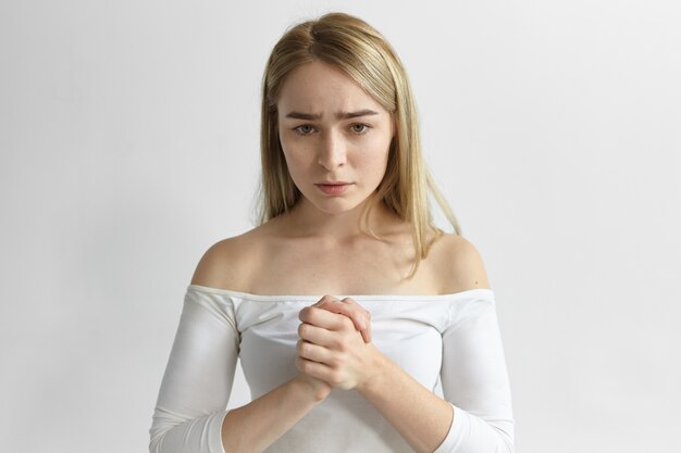 worried pensive young blonde woman with loose hairstyle rubbing hands, having uneasy look, worrying about her children, trying to concenrate and calm down. Body language