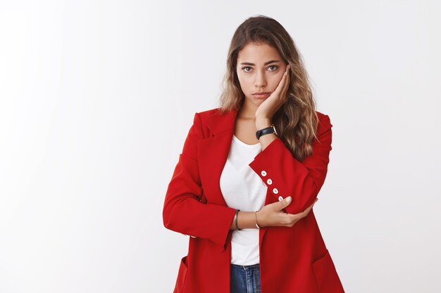 Worried perplexed troubled cute sad millennial 25s woman wearing red jacket facepalming, leaning head palm looking gloomy, upset camera failing, cannot solve situaton, standing white wall