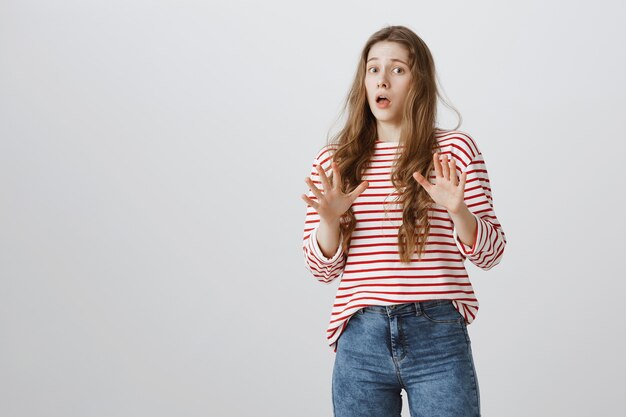 Worried scared girl raising hands up and step back startled