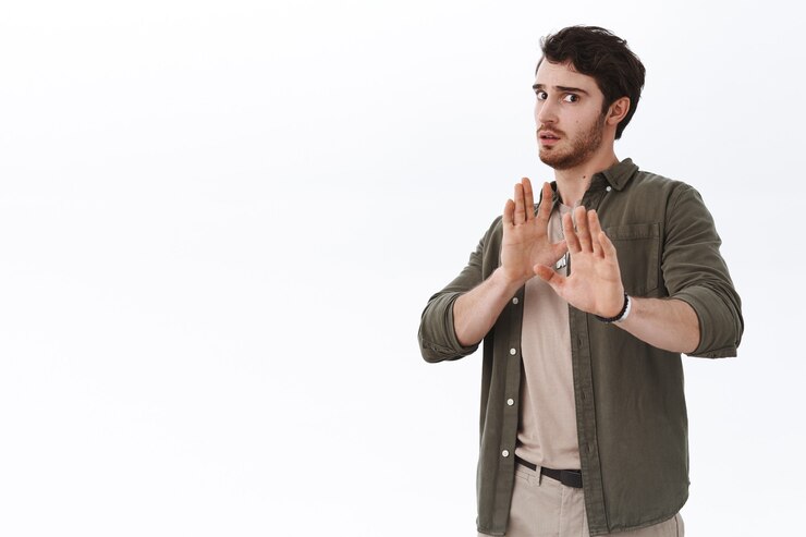 Free Photo worried and scared young handsome man avoiding fight. guy step back and raise hands in stop, refusal or defensive gesture
