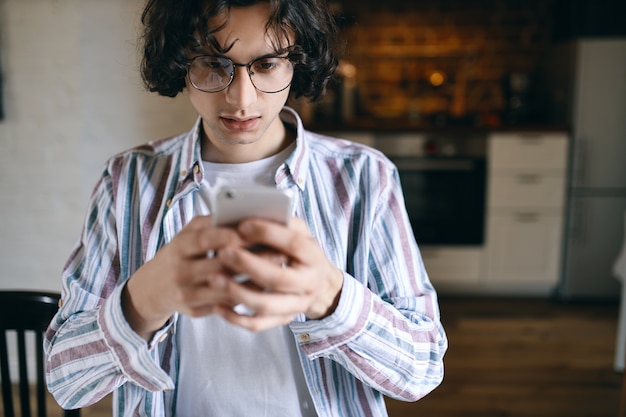 Giovane serio preoccupato che tiene telefono astuto, guardando lo schermo con espressione facciale frustrata, leggendo un messaggio di testo, ricevendo cattive notizie.