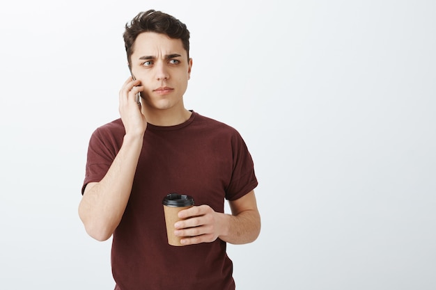 Worried suspicious attractive european man in casual red t-shirt talking by phone