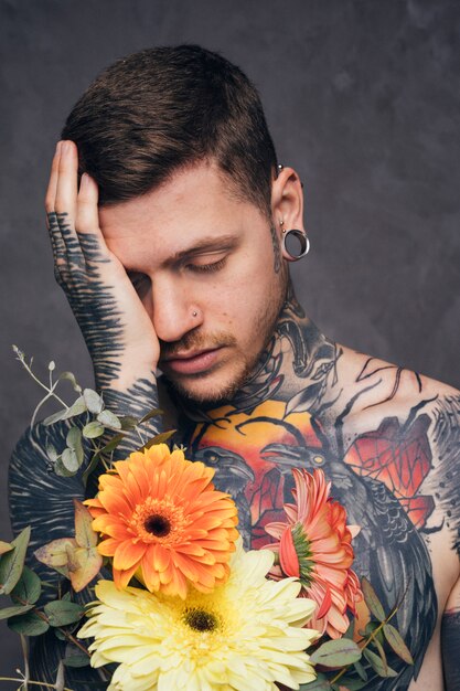 코와 귀 피어싱 꽃을 손에 들고 걱정 문신 된 젊은 남자