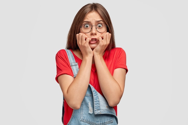 Free photo worried teenager with glasses posing against the white wall