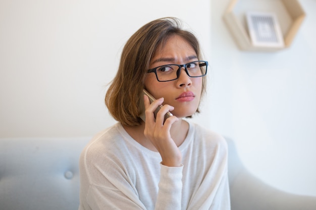 Worried woman calling on smartphone on sofa at home