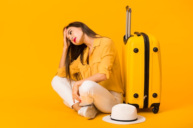 Worried woman posing next to luggage and hat