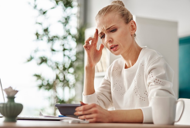 Worried woman with calculator at home office