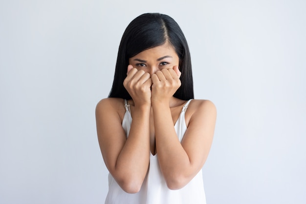 Worried young Asian woman covering mouth behind fists