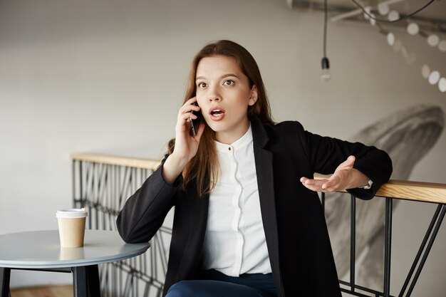 Worried young businesswoman at cafe talking by phone