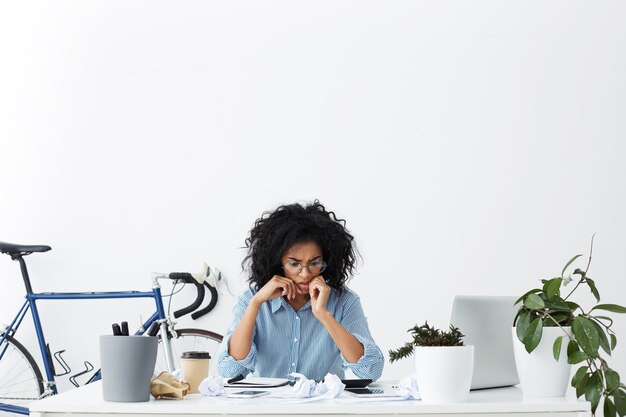 Worried young female office worker with curly hair having anxious desperate look