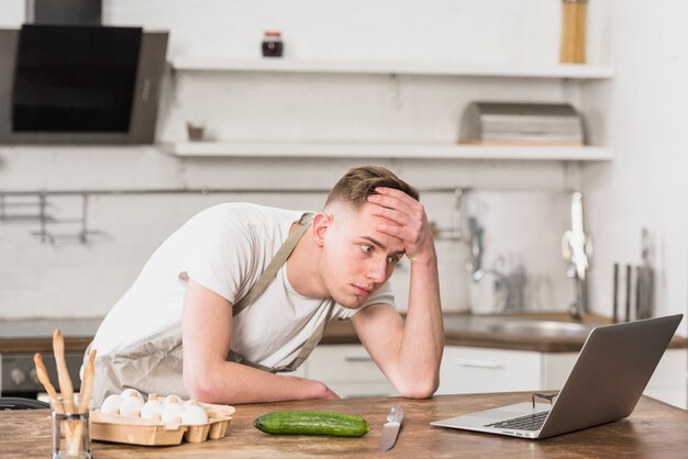 Worried young man with hand on his forehead looking at digital tablet